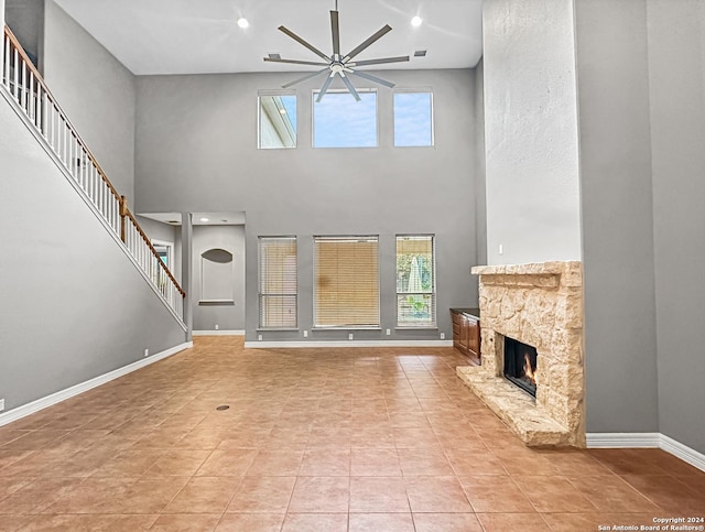 unfurnished living room featuring a stone fireplace, ceiling fan, a towering ceiling, and light tile patterned floors