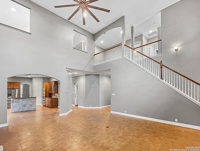 unfurnished living room featuring ceiling fan and a high ceiling