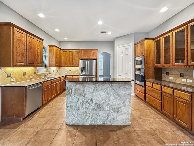 kitchen featuring appliances with stainless steel finishes, tasteful backsplash, sink, stone counters, and a center island