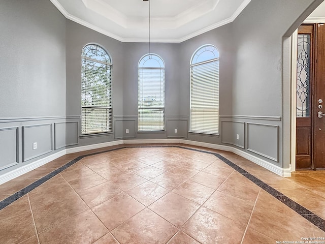 tiled empty room with crown molding and a tray ceiling