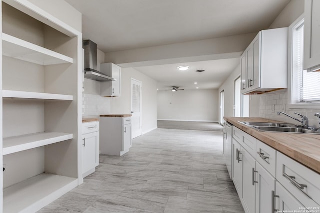 kitchen featuring ceiling fan, sink, wall chimney exhaust hood, butcher block countertops, and white cabinets