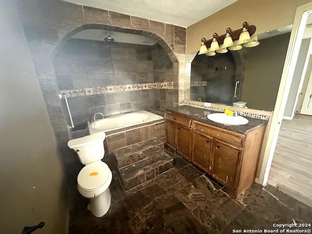 bathroom with tiled bath, hardwood / wood-style flooring, vanity, and toilet