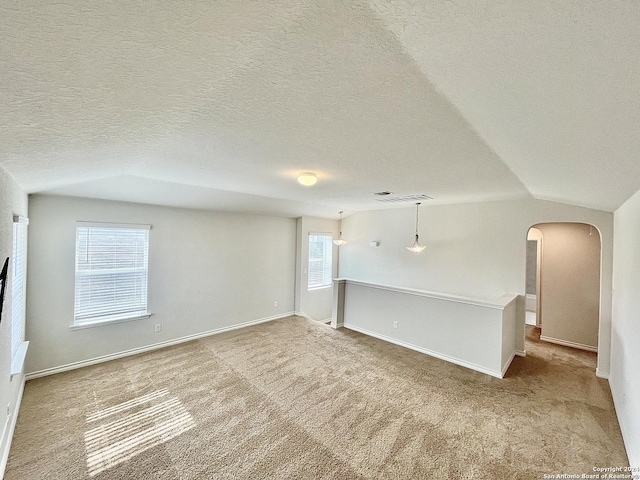 empty room with light colored carpet, lofted ceiling, and a textured ceiling