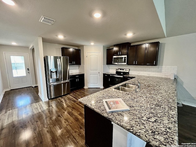 kitchen with dark brown cabinetry, light stone countertops, dark hardwood / wood-style floors, decorative backsplash, and appliances with stainless steel finishes