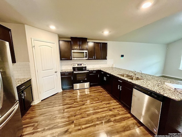 kitchen featuring sink, light stone countertops, appliances with stainless steel finishes, light hardwood / wood-style floors, and kitchen peninsula