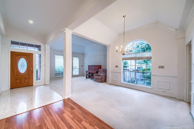 entrance foyer with crown molding, vaulted ceiling, ornate columns, light wood-type flooring, and a chandelier