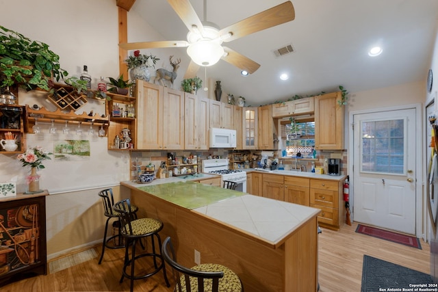 kitchen with a kitchen breakfast bar, kitchen peninsula, light hardwood / wood-style floors, lofted ceiling, and white appliances