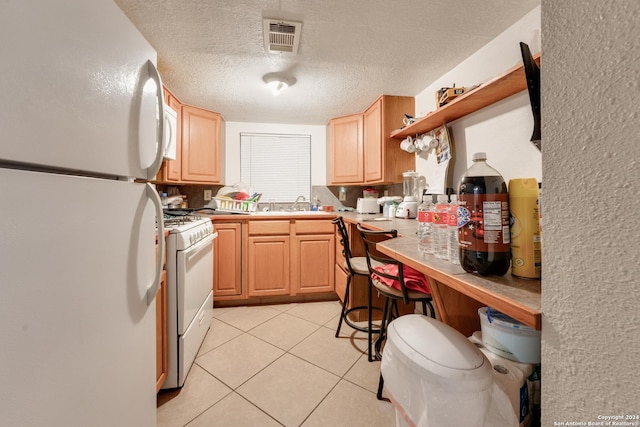 kitchen featuring light brown cabinets, sink, a textured ceiling, white appliances, and light tile patterned flooring