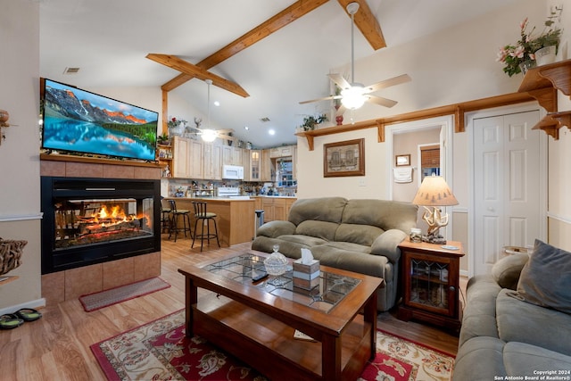 living room with beam ceiling, ceiling fan, light hardwood / wood-style flooring, high vaulted ceiling, and a tiled fireplace