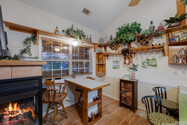 dining area featuring lofted ceiling, light wood-type flooring, and a tiled fireplace