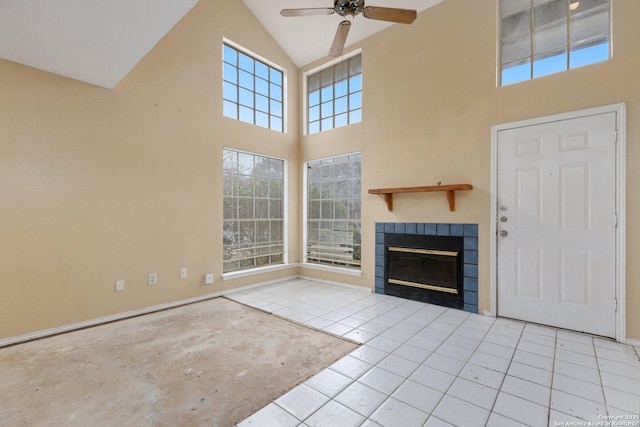 unfurnished living room with ceiling fan, light tile patterned floors, a fireplace, and a high ceiling