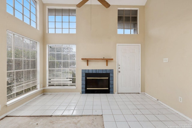 unfurnished living room with a tiled fireplace, ceiling fan, a towering ceiling, and light tile patterned flooring