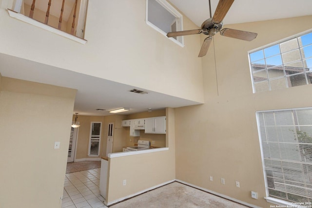 unfurnished living room with ceiling fan, light tile patterned flooring, and a high ceiling