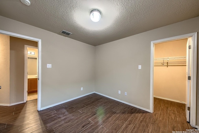 unfurnished bedroom featuring a spacious closet, a closet, dark wood-type flooring, and a textured ceiling