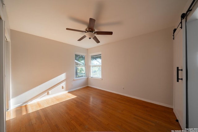 empty room with a barn door, ceiling fan, and hardwood / wood-style flooring