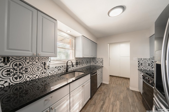 kitchen with dark stone counters, sink, hardwood / wood-style flooring, tasteful backsplash, and stainless steel appliances