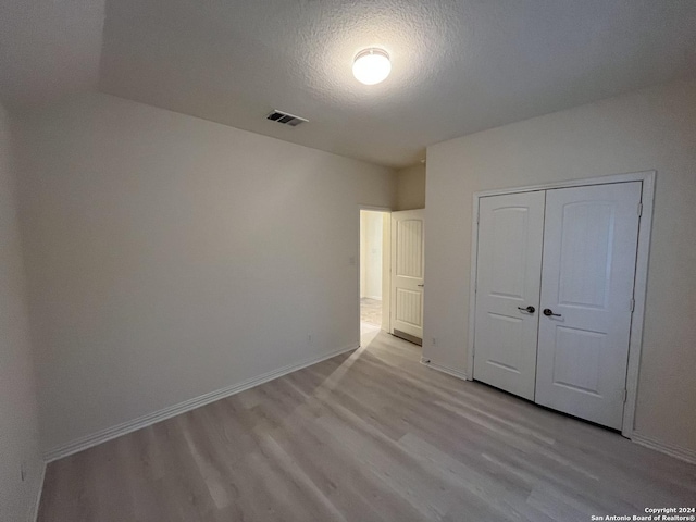 unfurnished bedroom with a textured ceiling, light hardwood / wood-style flooring, and a closet