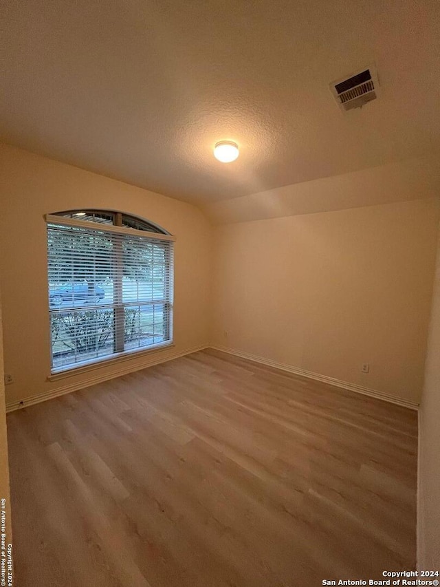 empty room featuring hardwood / wood-style floors, a textured ceiling, and vaulted ceiling