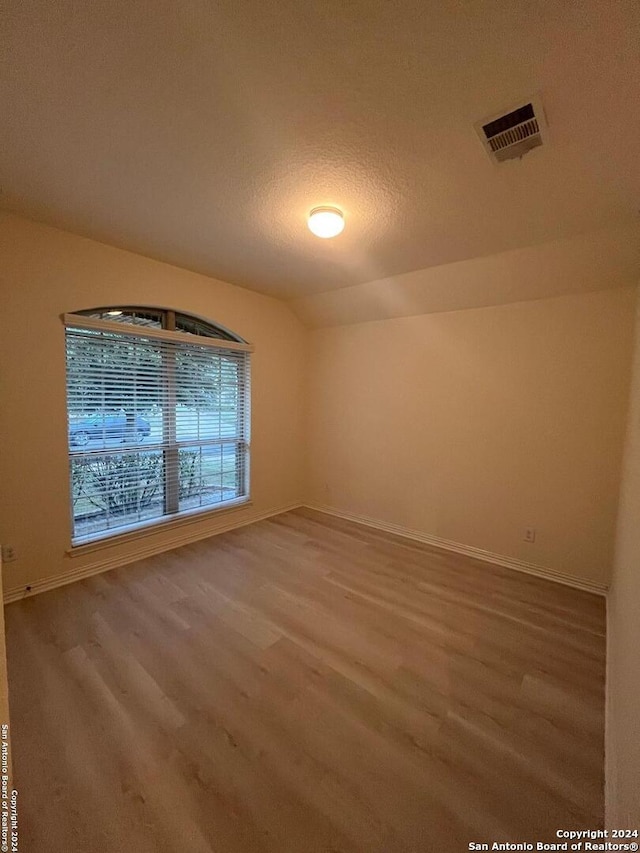 unfurnished room with hardwood / wood-style floors, a textured ceiling, and vaulted ceiling