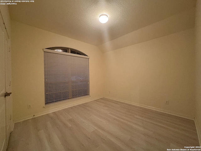 spare room featuring vaulted ceiling, light hardwood / wood-style floors, and a textured ceiling