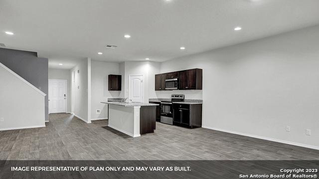 kitchen with dark brown cabinetry, an island with sink, wood-type flooring, and appliances with stainless steel finishes