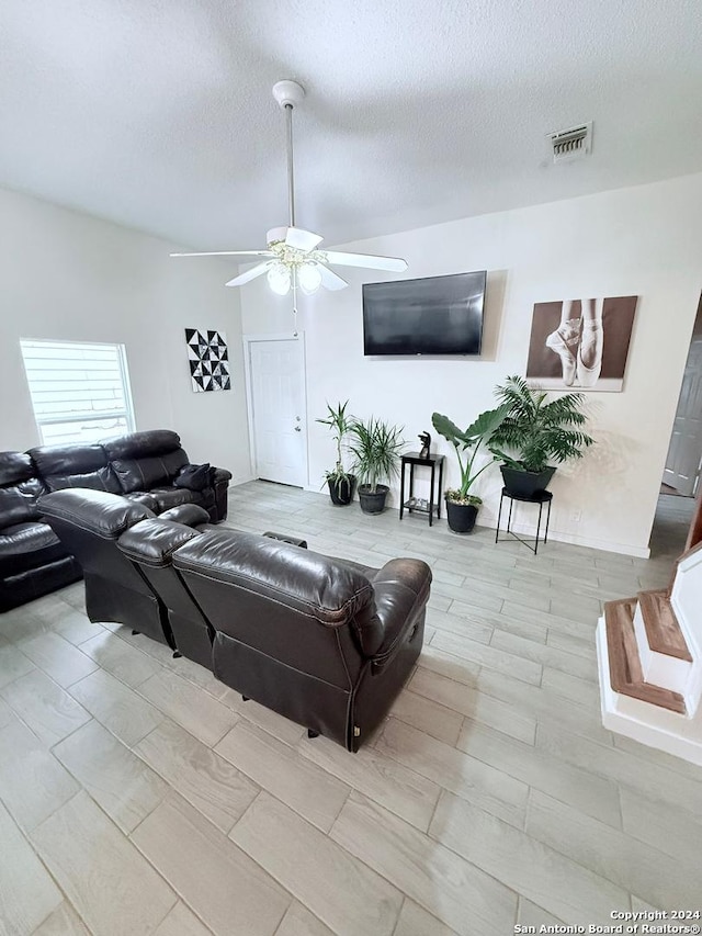 living room featuring light wood-type flooring, a textured ceiling, and ceiling fan