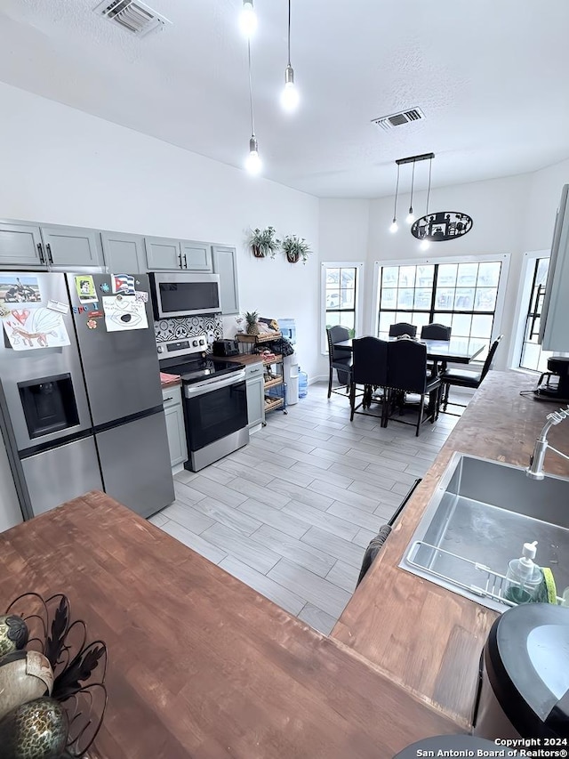 kitchen with pendant lighting, sink, light hardwood / wood-style flooring, gray cabinets, and appliances with stainless steel finishes