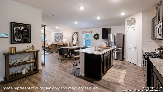 kitchen with tasteful backsplash, a center island with sink, stainless steel appliances, and wood-type flooring