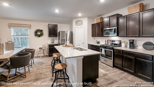 kitchen with sink, backsplash, light hardwood / wood-style floors, a kitchen island with sink, and appliances with stainless steel finishes