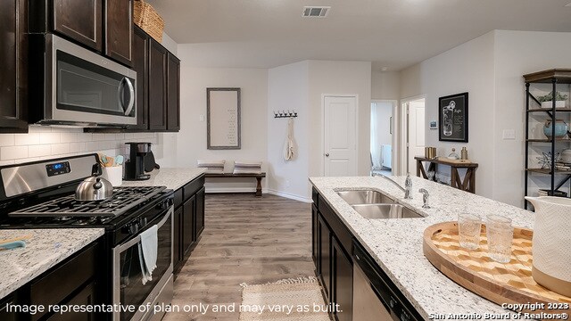 kitchen with light stone countertops, appliances with stainless steel finishes, tasteful backsplash, sink, and light hardwood / wood-style flooring