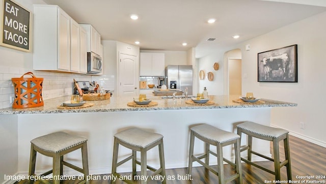 kitchen with light stone countertops, a kitchen breakfast bar, dark hardwood / wood-style flooring, white cabinets, and appliances with stainless steel finishes