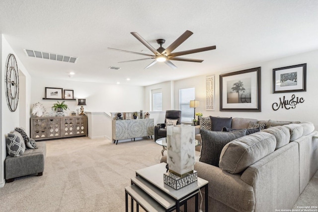 living room featuring ceiling fan, light colored carpet, and a textured ceiling