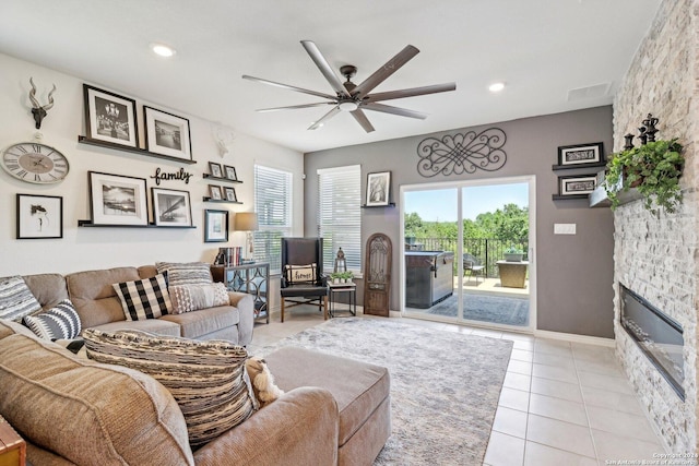 living room featuring a stone fireplace, ceiling fan, and light tile patterned floors