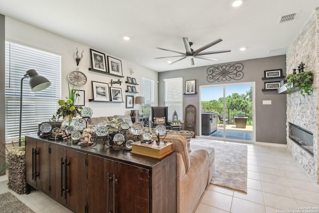 living room with a stone fireplace, ceiling fan, and light tile patterned floors