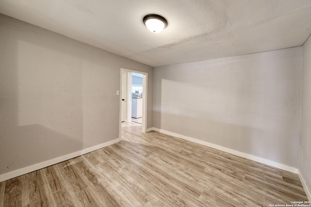 empty room featuring a textured ceiling, light hardwood / wood-style floors, and washer / clothes dryer