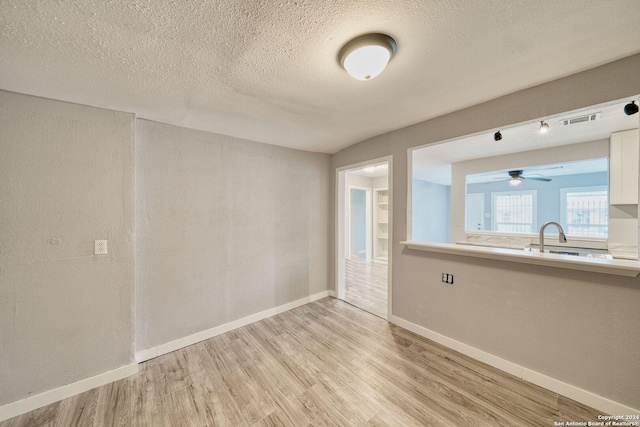 empty room with a textured ceiling, light hardwood / wood-style flooring, ceiling fan, and sink