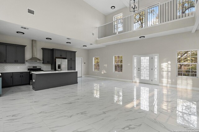 kitchen with wall chimney exhaust hood, stainless steel appliances, a high ceiling, decorative backsplash, and a kitchen island