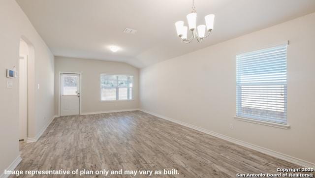 spare room with hardwood / wood-style flooring, vaulted ceiling, and an inviting chandelier