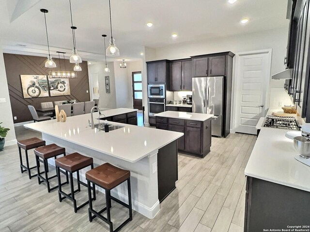 kitchen with appliances with stainless steel finishes, a spacious island, sink, decorative light fixtures, and a breakfast bar area