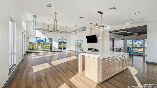 kitchen with pendant lighting, dark wood-type flooring, light brown cabinetry, a large island, and a large fireplace