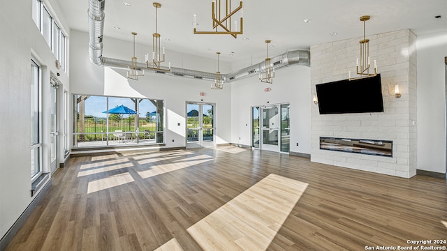 unfurnished living room with a large fireplace, a towering ceiling, wood-type flooring, and french doors