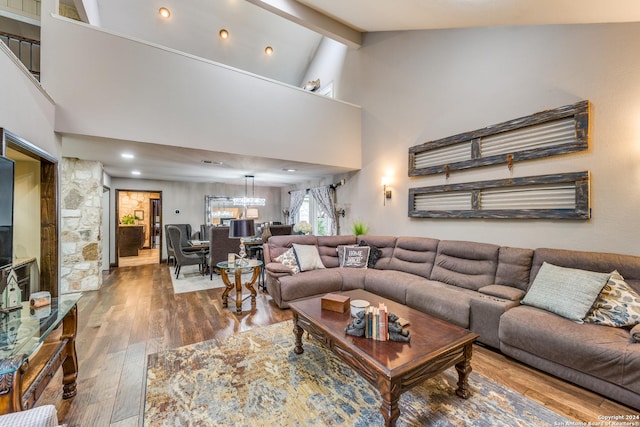 living room featuring beam ceiling, hardwood / wood-style floors, high vaulted ceiling, and a chandelier