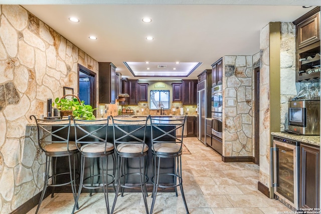 kitchen with a breakfast bar area, beverage cooler, kitchen peninsula, a tray ceiling, and decorative backsplash