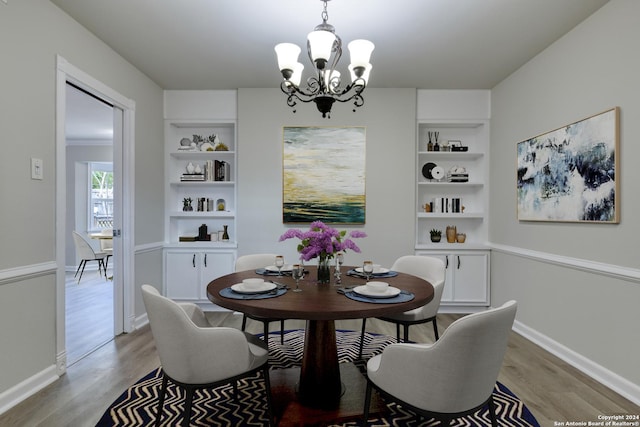 dining room with built in features, light wood-type flooring, and an inviting chandelier