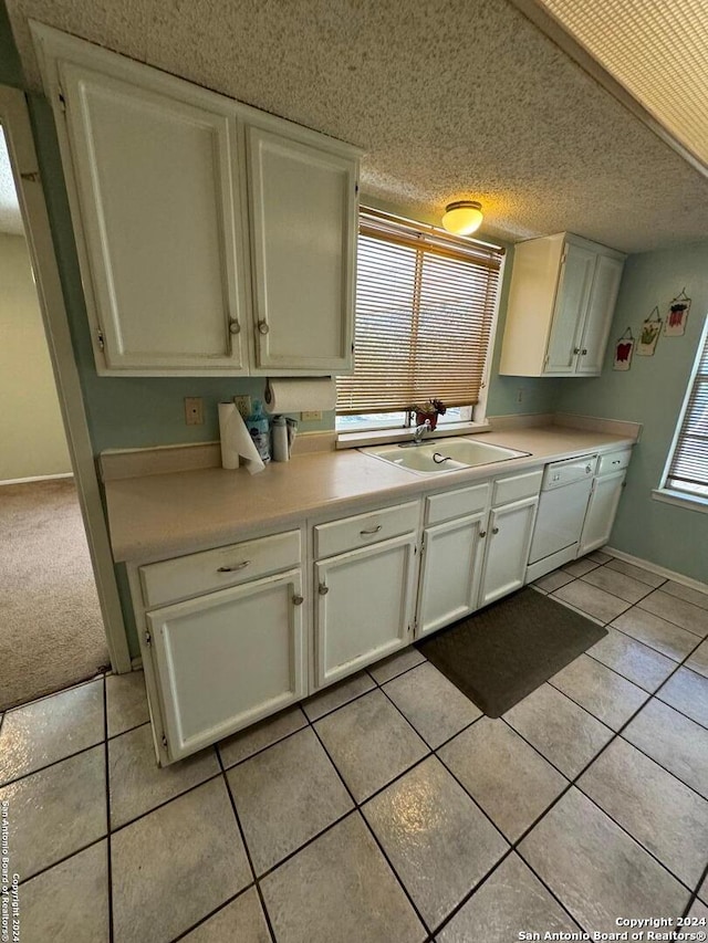 kitchen with light tile patterned floors, white dishwasher, white cabinetry, and sink