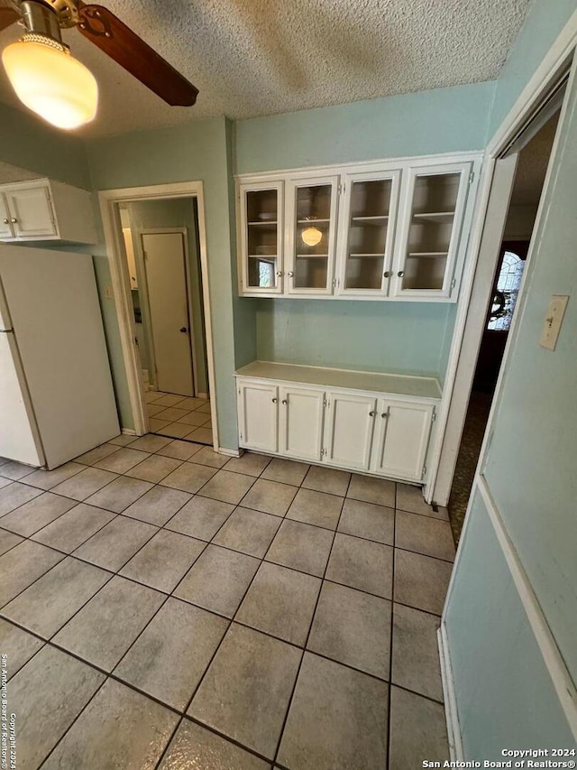 unfurnished dining area featuring ceiling fan, light tile patterned flooring, and a textured ceiling