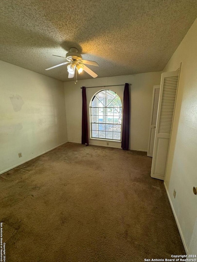 empty room featuring dark colored carpet, a textured ceiling, and ceiling fan