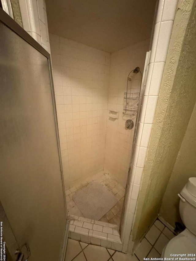 bathroom with tile patterned flooring, a tile shower, and toilet