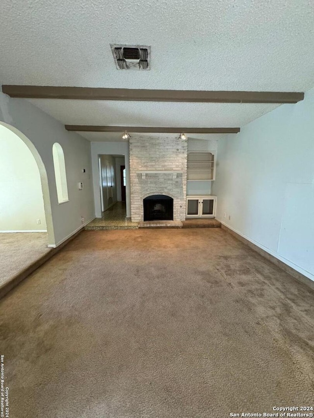 unfurnished living room featuring carpet flooring, a fireplace, beamed ceiling, and a textured ceiling