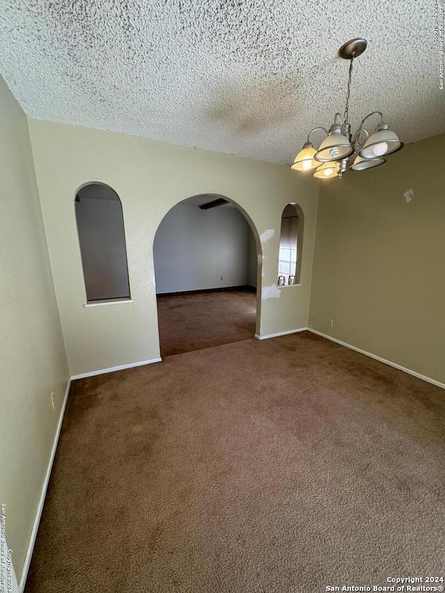 carpeted empty room featuring a textured ceiling and an inviting chandelier